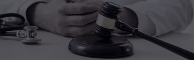 A person with folded hands sits at a desk with a gavel and a stethoscope placed in front, symbolizing the intersection of law and medicine.