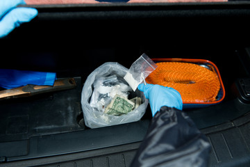 gloved hands with bag of drugs in trunk of car