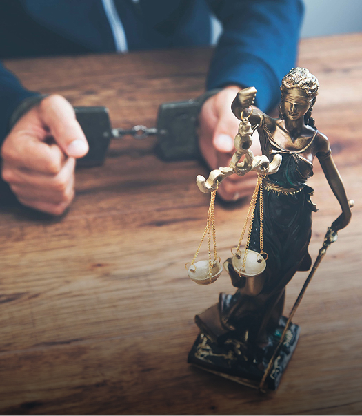 man in handcuffs across from a statue of lady justice